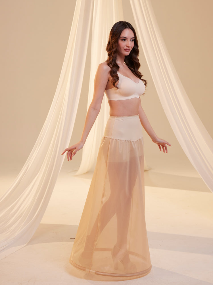 A woman wearing a white A-line wedding dress with a hoop underskirt and a waist corsage, standing in a flowing pose.